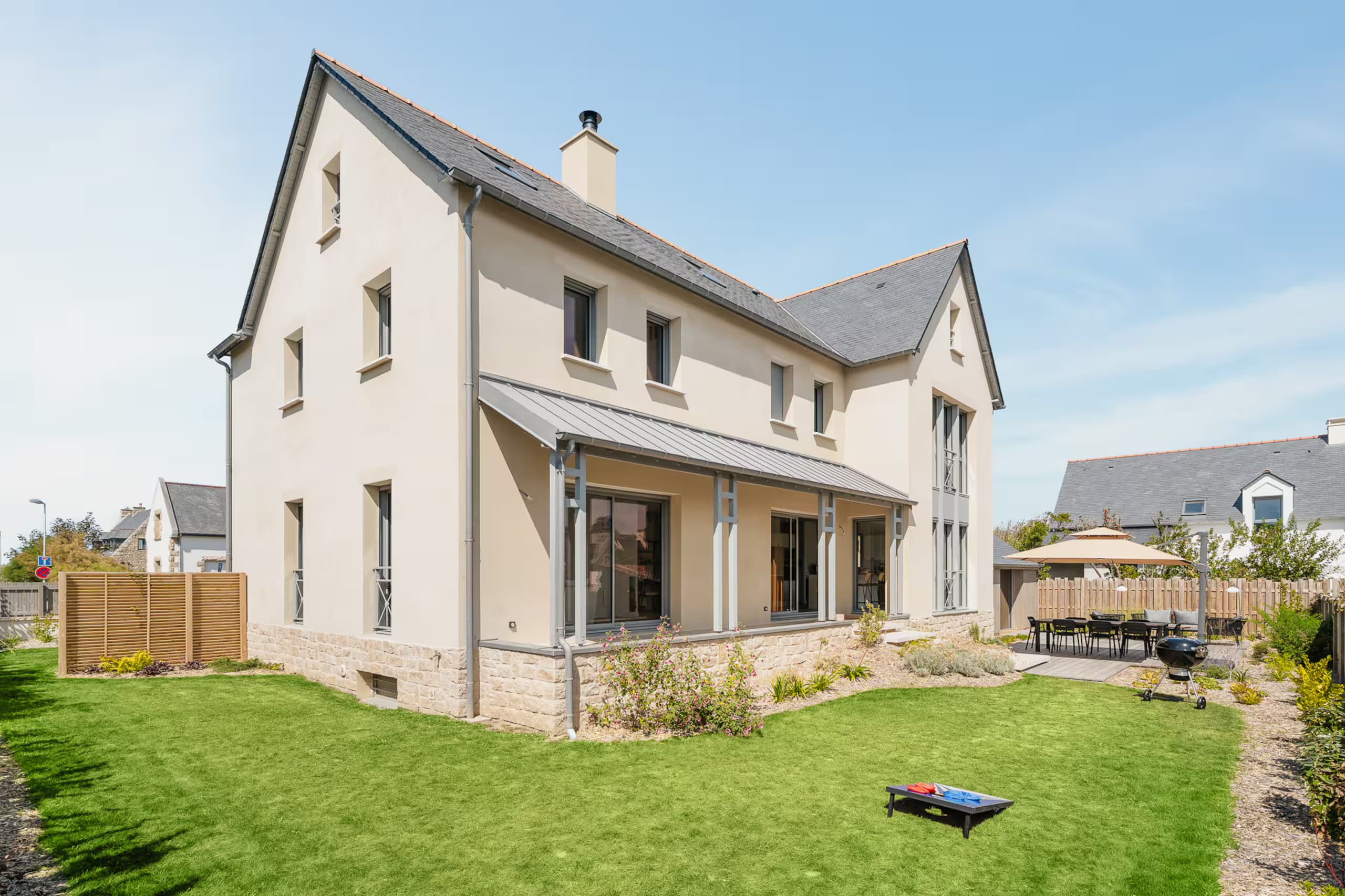 Façade arrière de la villa et sa pelouse, sous un ciel bleu